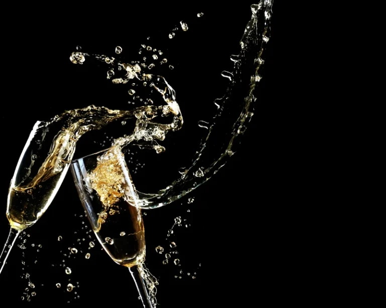 To glas med champagne, der skåler, med sprøjt af væske og bobler mod en sort baggrund.